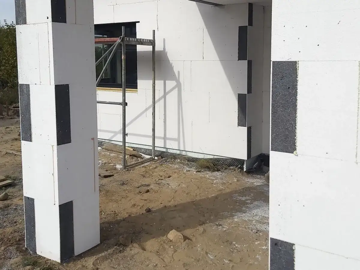 Budowa domu z bloczków styropianowych. Czy trzeba kołkować styropian grafitowy? Widok na fragment ściany i słupa z szarego styropianu.
