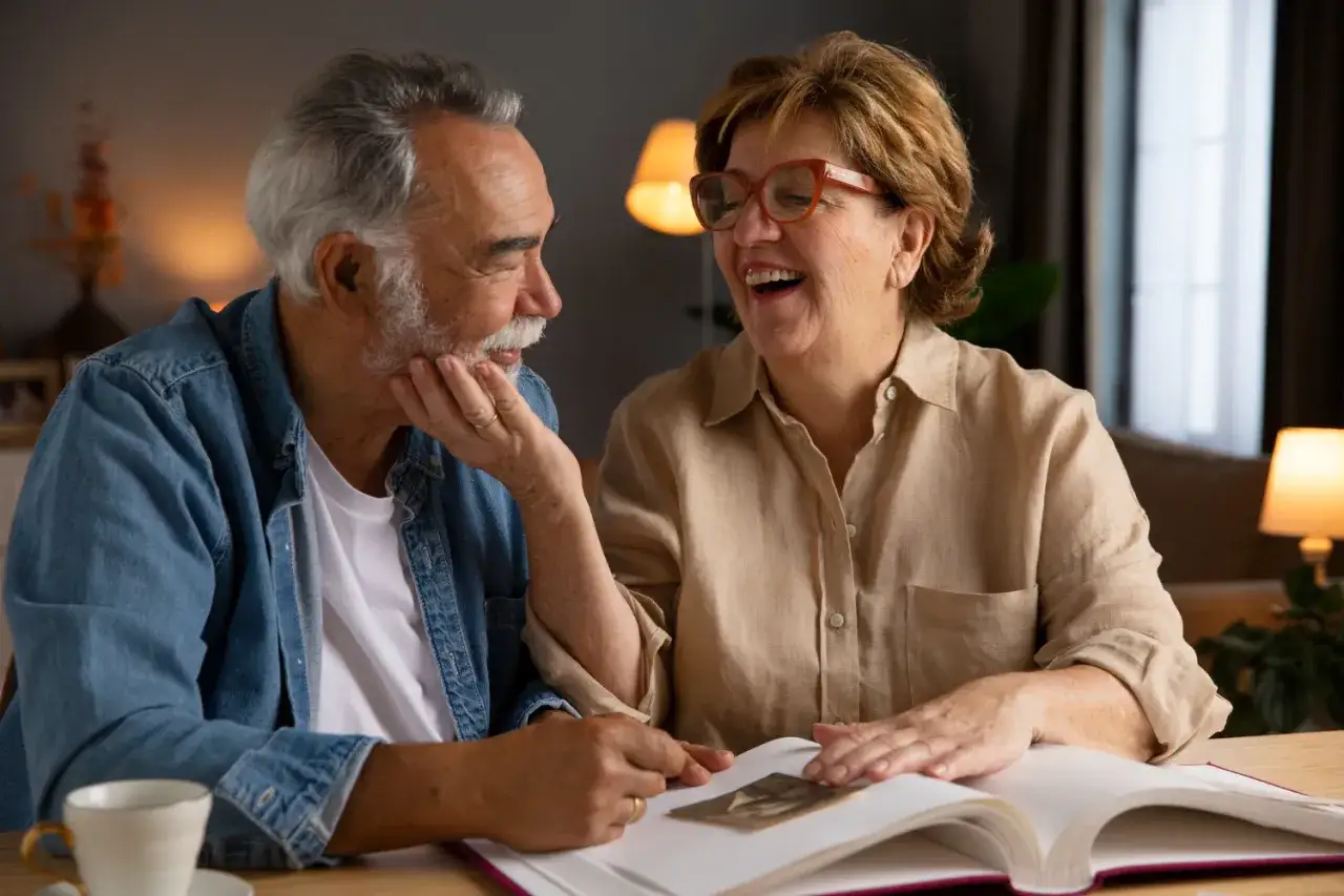 Para starsza para przegląda album ze zdjęciami, śmiejąc się. Czy opieka nad starszą osobą wlicza się do lat pracy?
