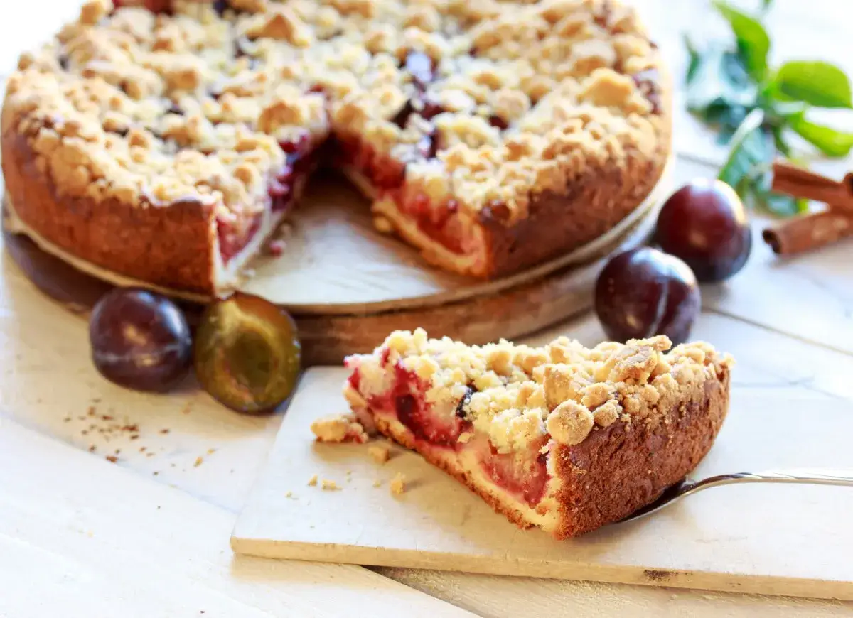 Pyszne ciasto ze śliwkami i kruszonką, idealne do przepisów z kruchego ciasta. Obok leżą świeże śliwki i laski cynamonu.