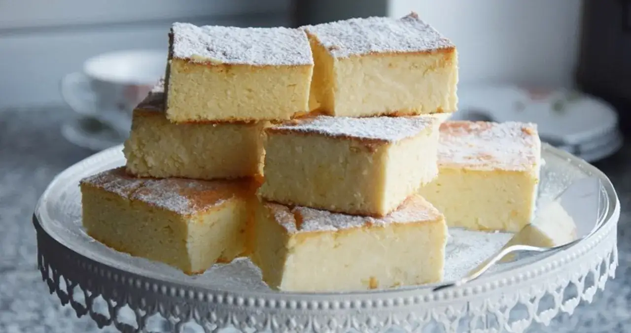 Sernik bez spodu, który zawsze się udaje, pokrojony w kostkę i posypany cukrem pudrem, ułożony na paterze.