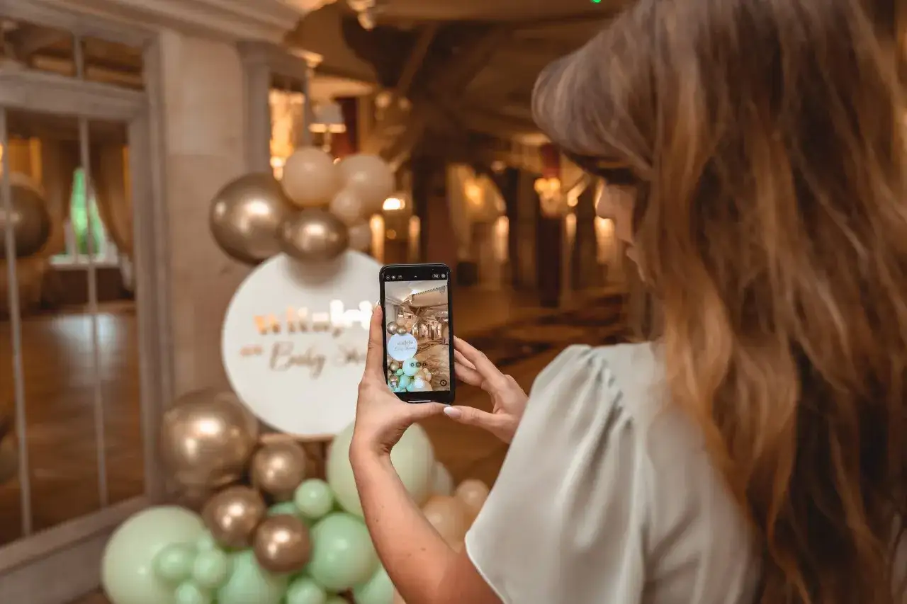 Kobieta robi zdjęcie dekoracji na baby shower. Złote i miętowe balony tworzą łuk. Świetne baby shower pomysły!