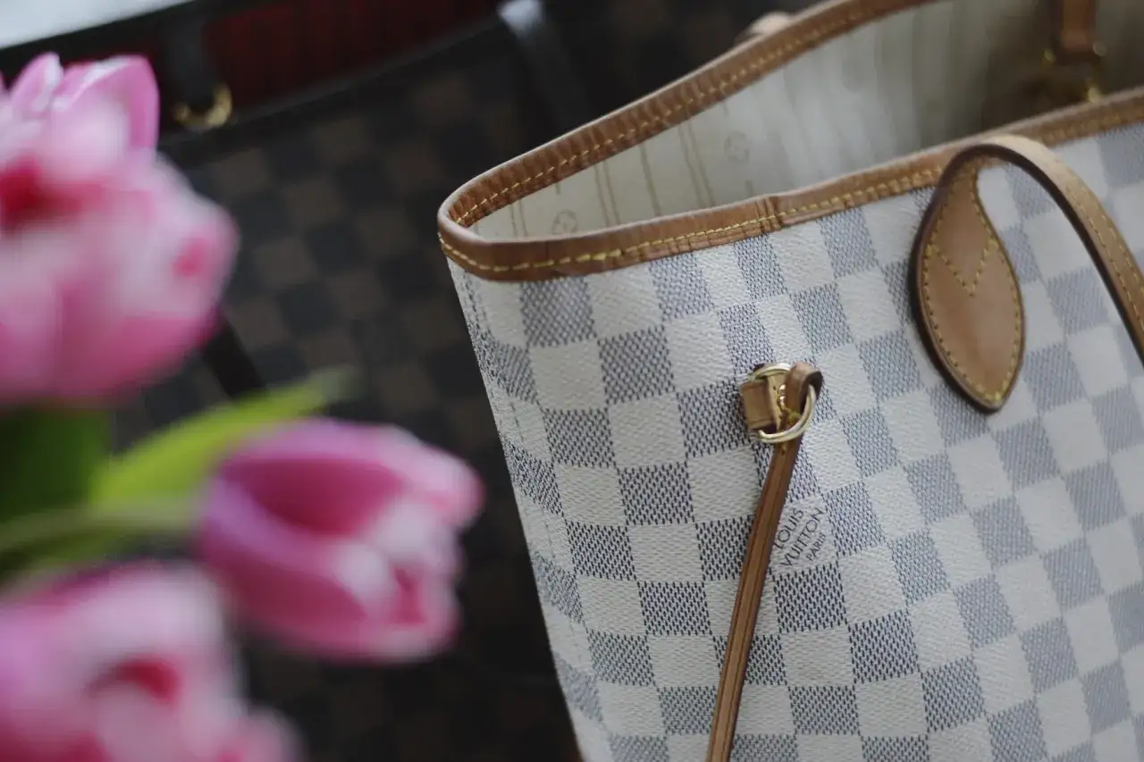 Jasna torebka Louis Vuitton w kratkę Damier Azur z różowymi tulipanami w tle.
