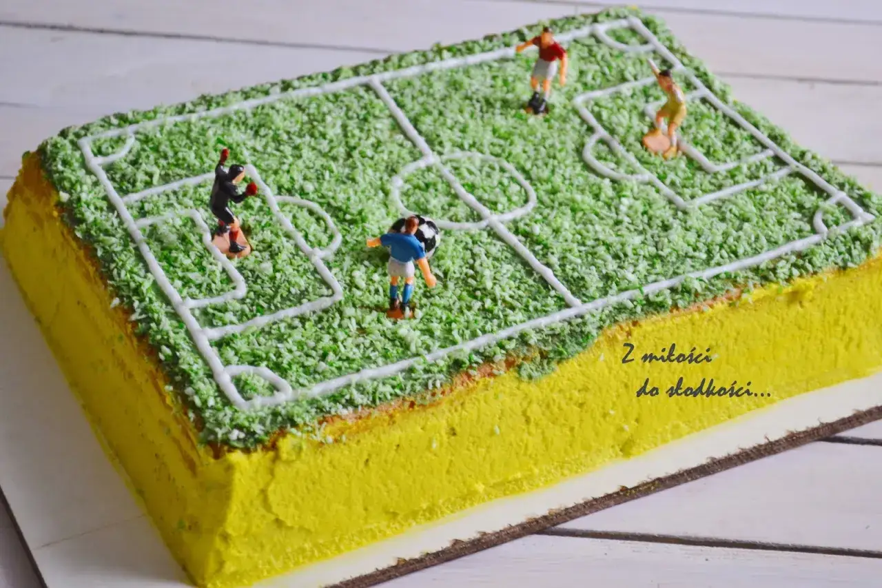 Jak zrobić tort boisko do piłki nożnej? Zielona posypka imituje trawę, a białe linie wyznaczają pole gry. Figurki piłkarzy i piłka dodają realizmu.