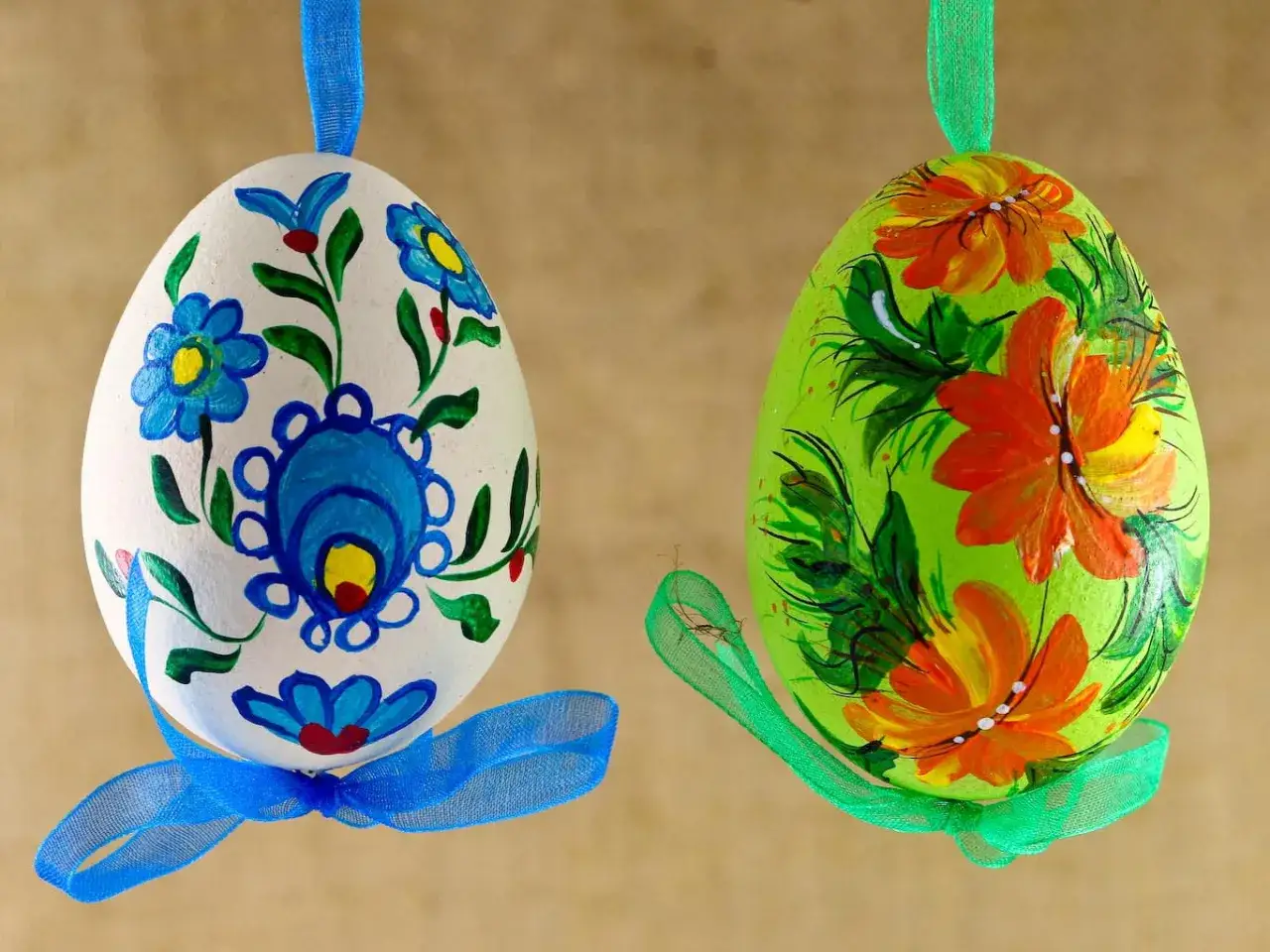 Dwa ręcznie malowane pisanki wielkanocne wzory: biała z niebieskimi kwiatami i zielona z pomarańczowymi.