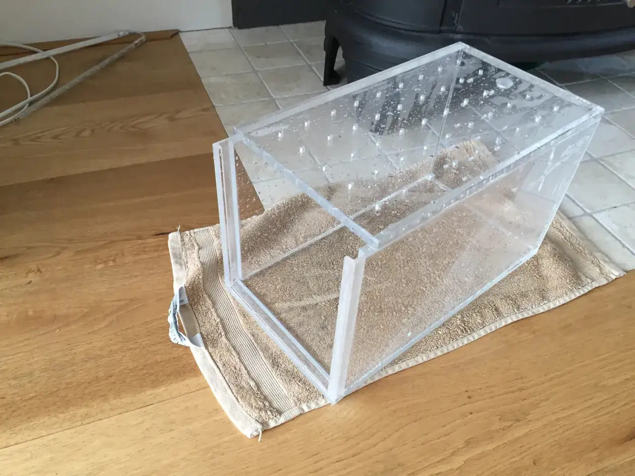 Przezroczysty pojemnik z otworami, na ręczniku, może posłużyć do eksperymentów, jak zrobić pułapkę na ryby.