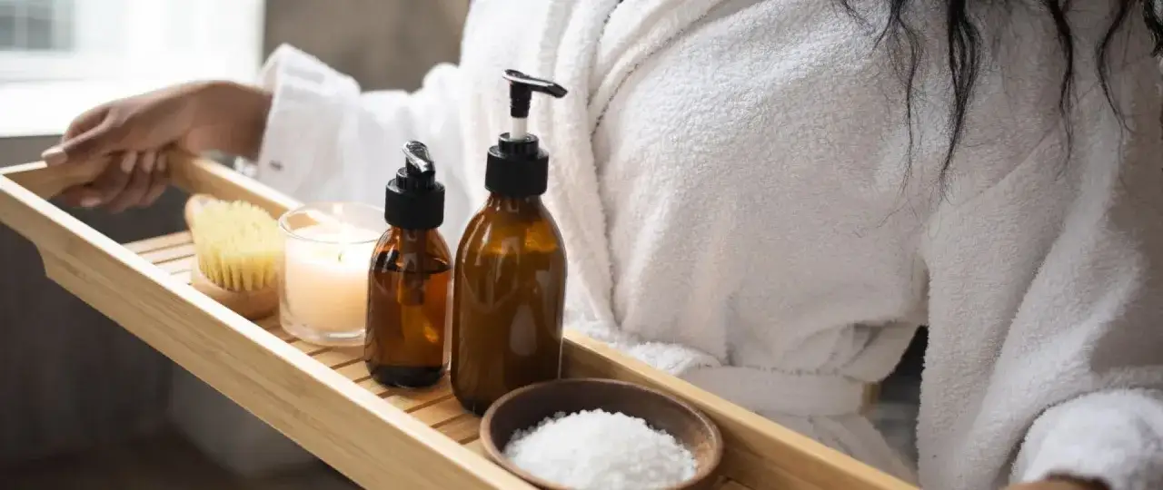 Drewniana taca z kosmetykami do kąpieli: świeca, olejki, sól i szczotka.