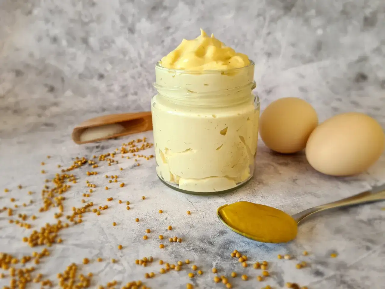 Domowy majonez dietetyczny w słoiku, jajka, musztarda na łyżce i nasiona gorczycy. Proste składniki do przygotowania pysznego sosu.