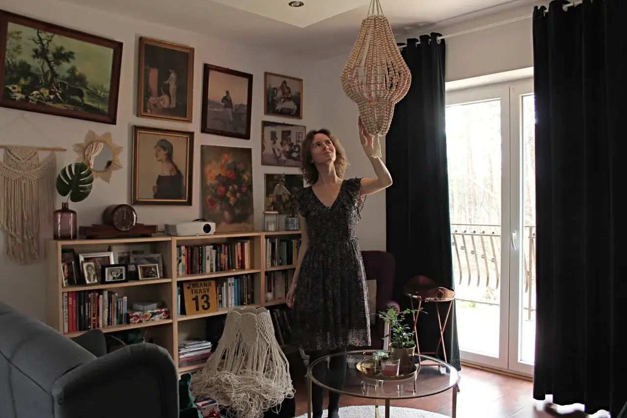 Kobieta w salonie z książkami i obrazami na ścianach, zastanawia się, jak samemu odnowić żyrandol z koralików.