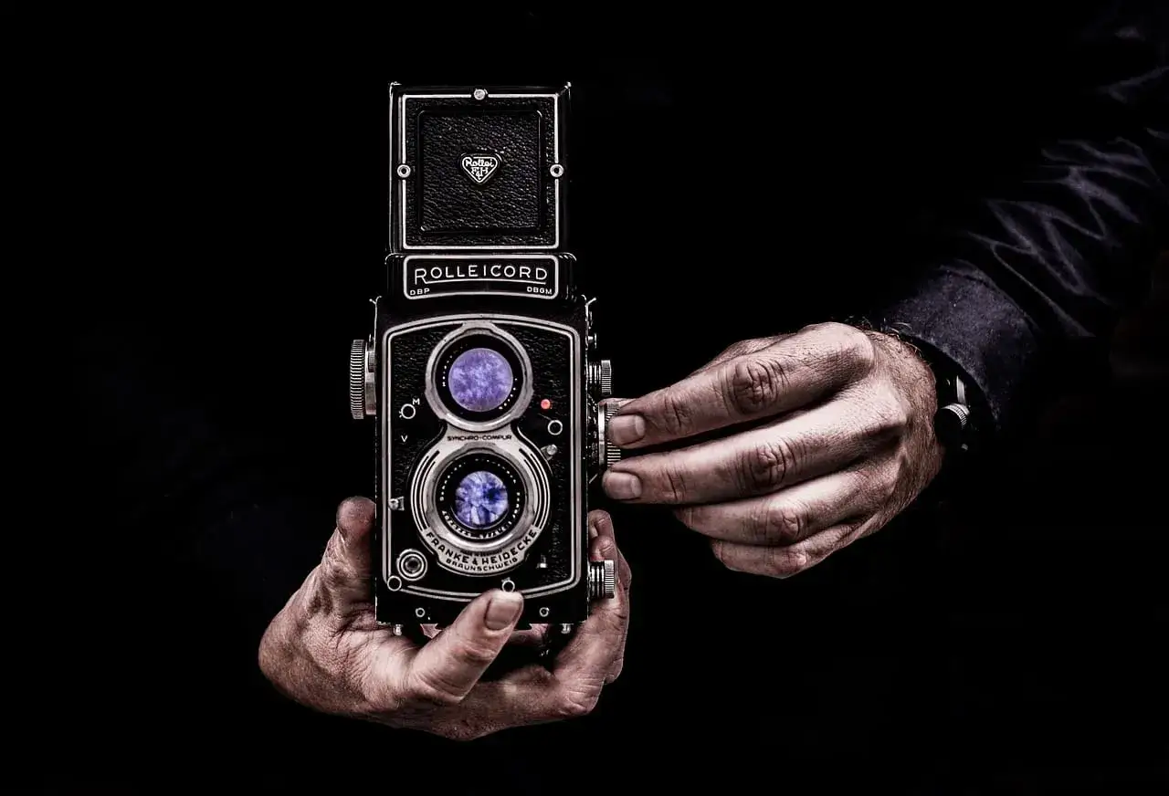 Dwie ręce trzymają aparat Rolleiflex, jedna reguluje ostrość. Sztuka fotografii, zasada złotego środka w kadrze.