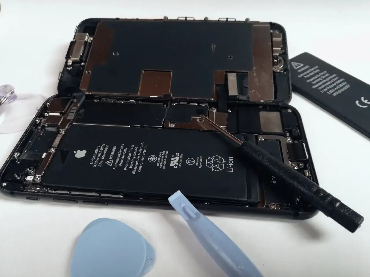 Rozłożony iPhone 8 z widoczną baterią i narzędziami do naprawy.