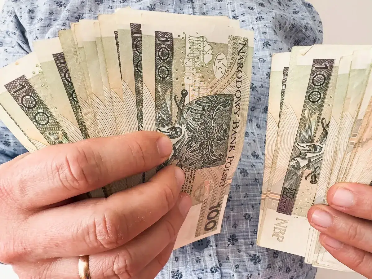 Ręce trzymające plik banknotów 100 zł. Planowanie finansowe, jak wybrać najkorzystniejsze lata do emerytury, wymaga analizy oszczędności.