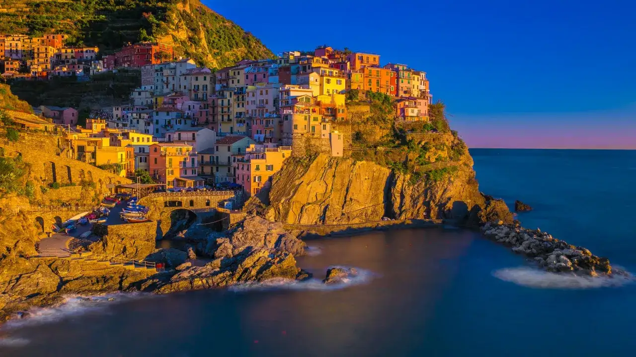 Kolorowe domy Cinque Terre w **Włoszech we wrześniu**, oświetlone złotym słońcem, schodzą ku morzu.