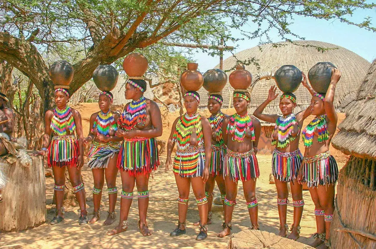 Kobiety w tradycyjnych strojach niosą dzbanki na głowach. Scena z królestwa Eswatini.