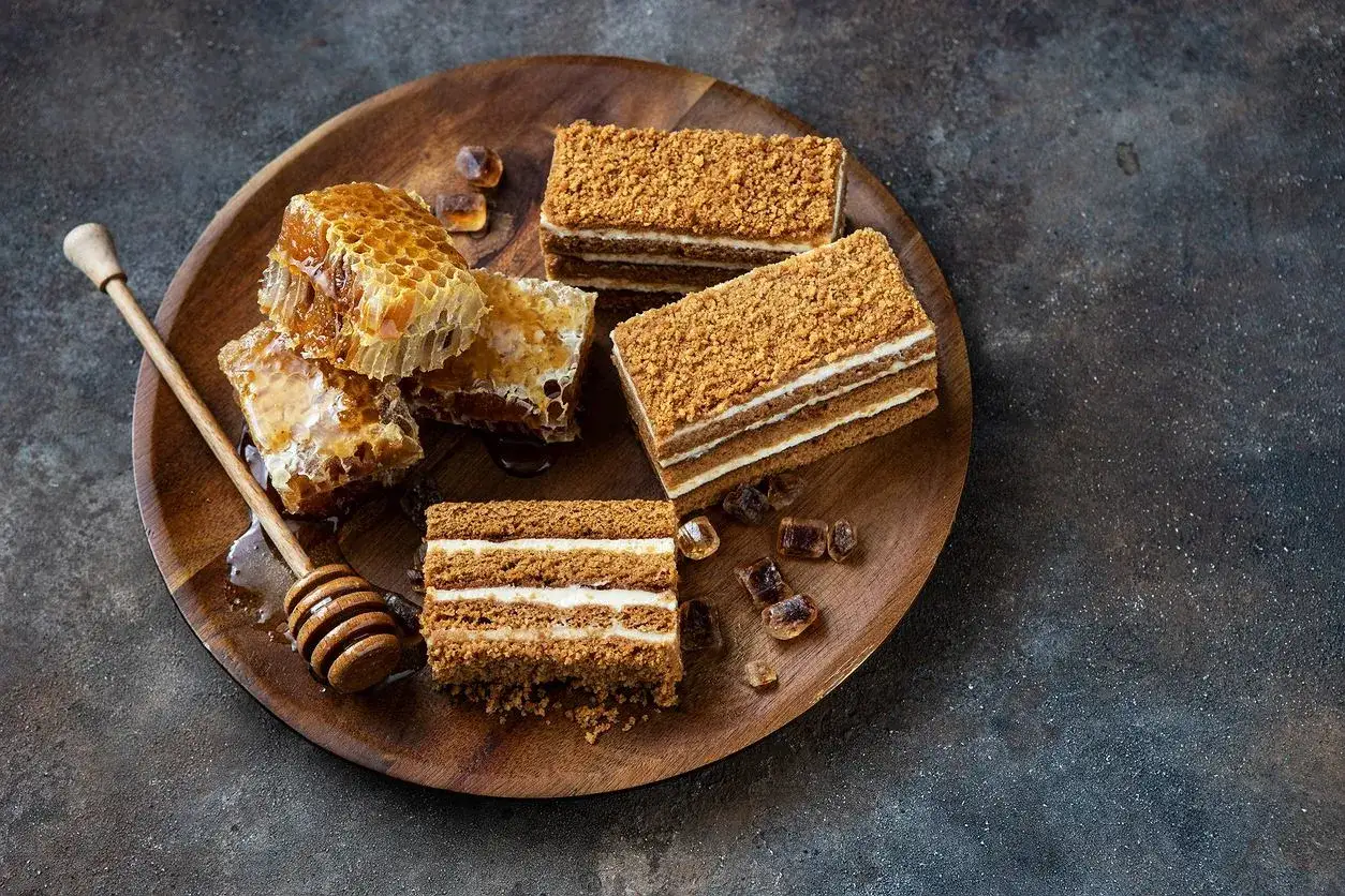 Plaster miodowy z kremem i plastry miodu na drewnianej tacy.