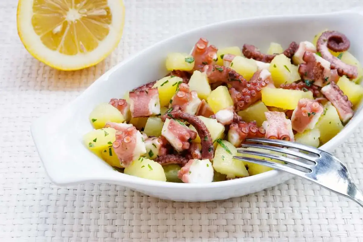 Octopus and potato salad with lemon and parsley in a white bowl.
