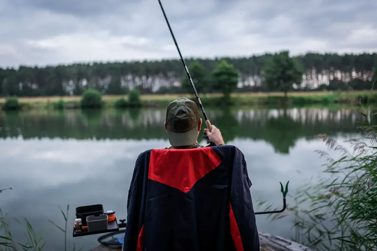 Wędkarz z klasycznym feederem czeka na branie nad spokojnym jeziorem. Jaka wędka do klasycznego feedera? Ta wydaje się idealna.