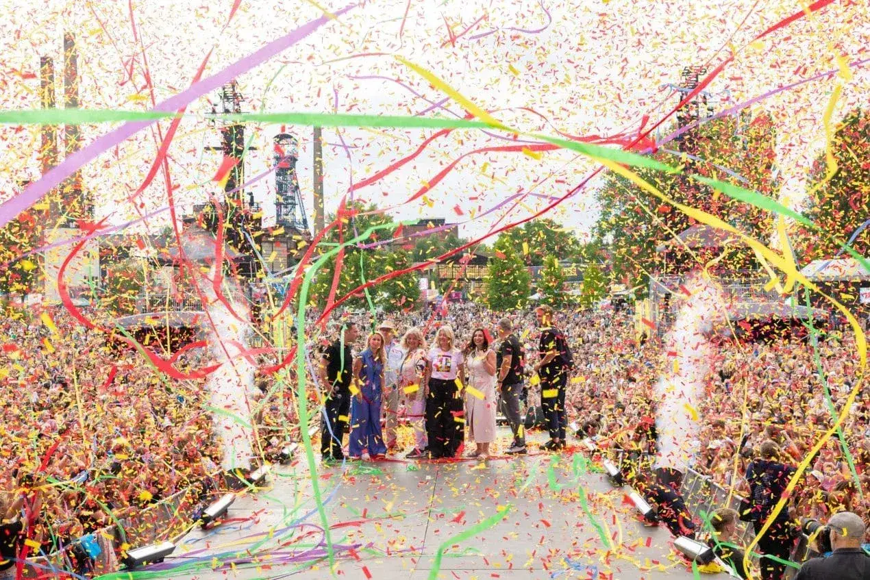 Tłum wiwatuje, a konfetti w żywych barwach, symbolizujące kolory Ostrawy, spada na scenę, gdzie stoi grupa ludzi.