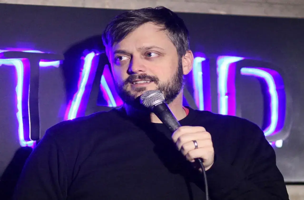 Mężczyzna z mikrofonem na tle neonowego napisu "STAND UP".