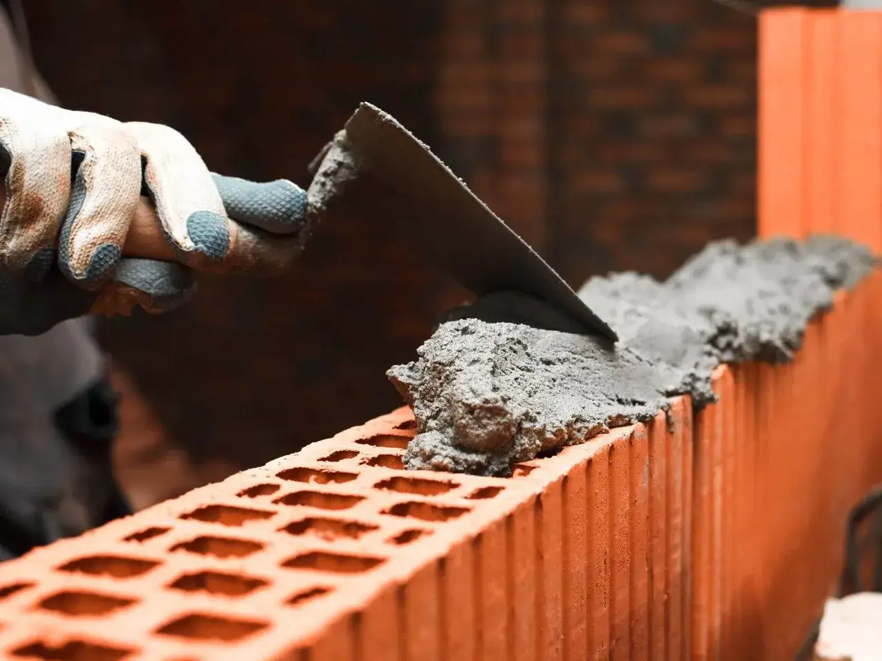 Murarz nakłada zaprawę na pustaki. Zastanawiasz się, ile kosztuje worek zaprawy murarskiej?
