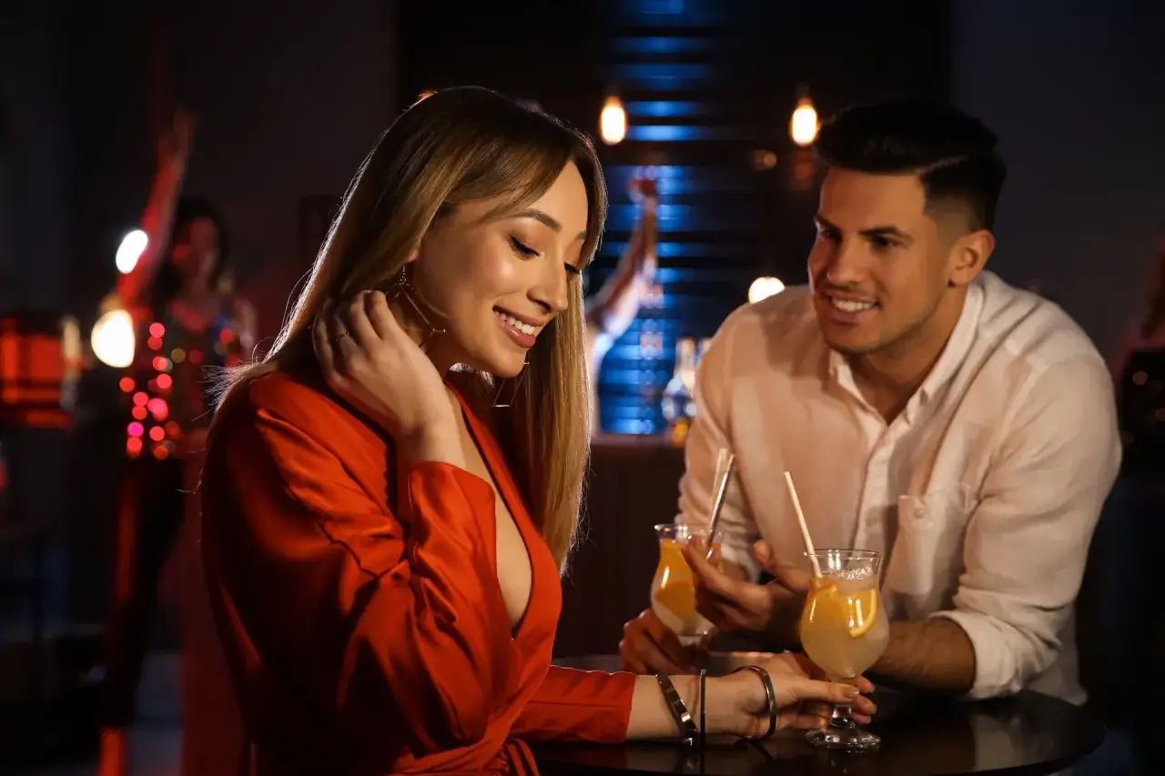 Uśmiechnięta kobieta w czerwonej sukience i mężczyzna przy drinkach. Czy to jej triki działające na mężczyzn?