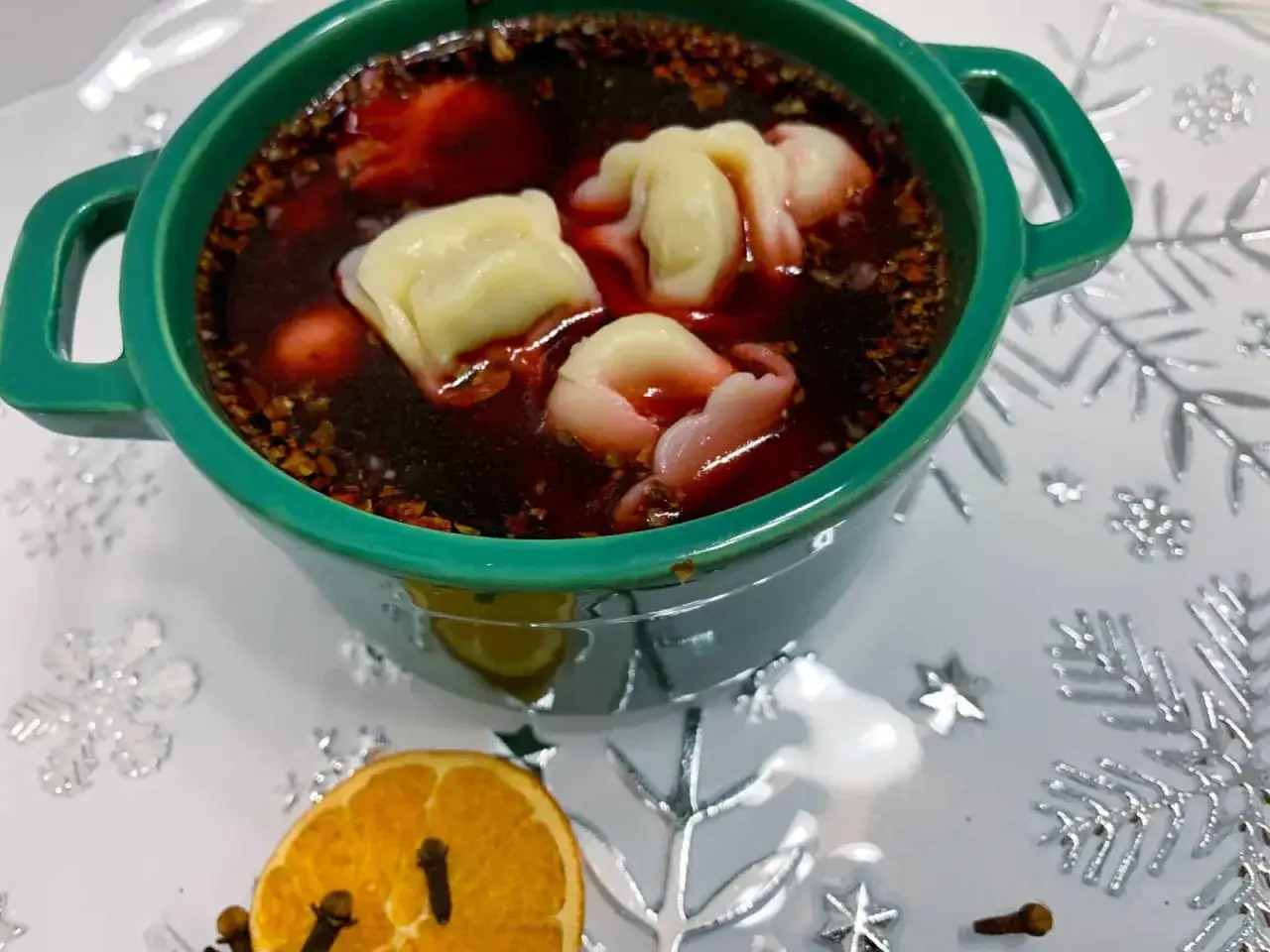 Aromaticzny barszcz z uszkami w zielonej miseczce, ozdobiony suszoną pomarańczą i goździkami.