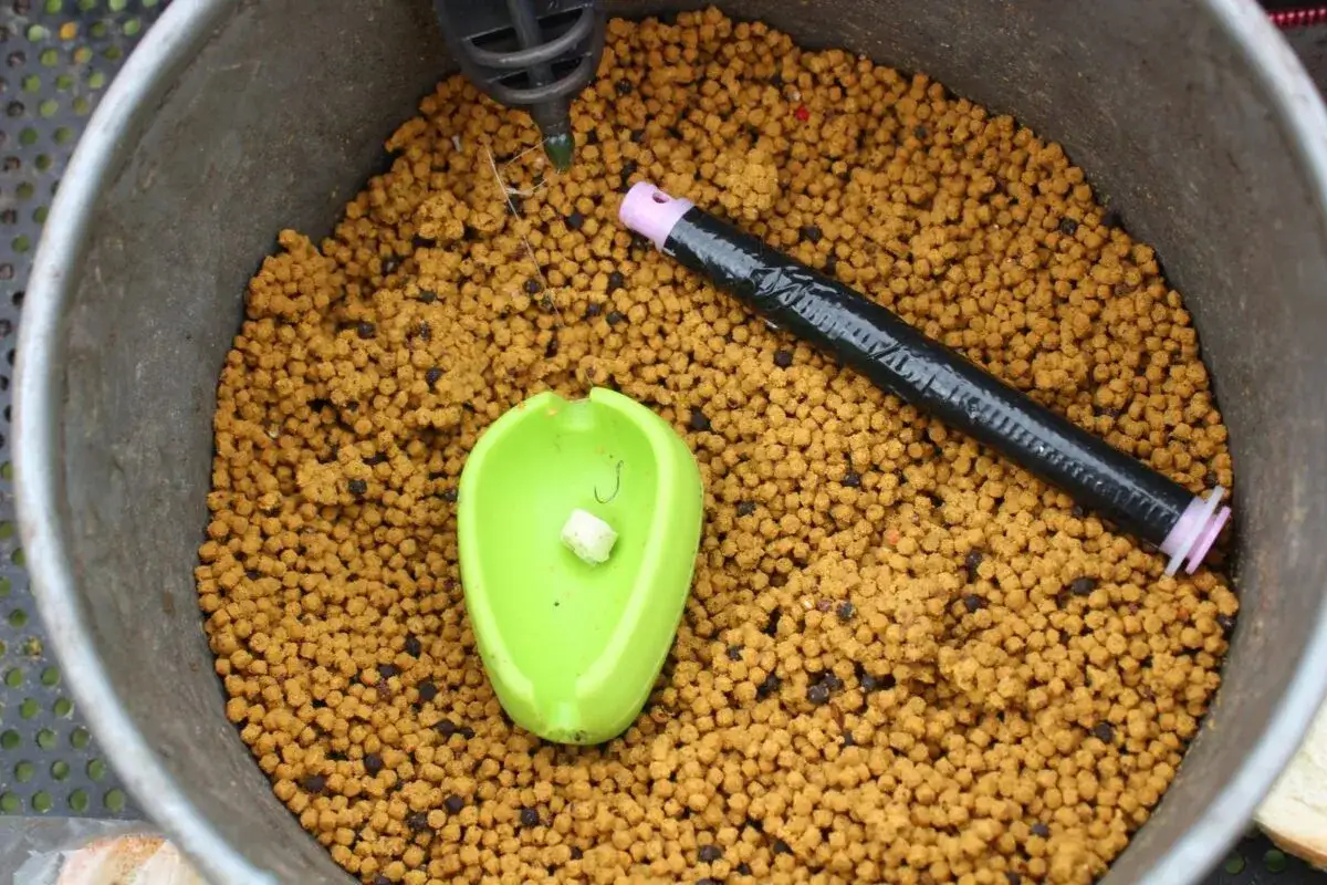 Wiadro z zanętą, zielona łyżka z haczykiem i kawałkiem chleba, czarny tubus. To wszystko, by pokazać, jak założyć chleb na haczyk.