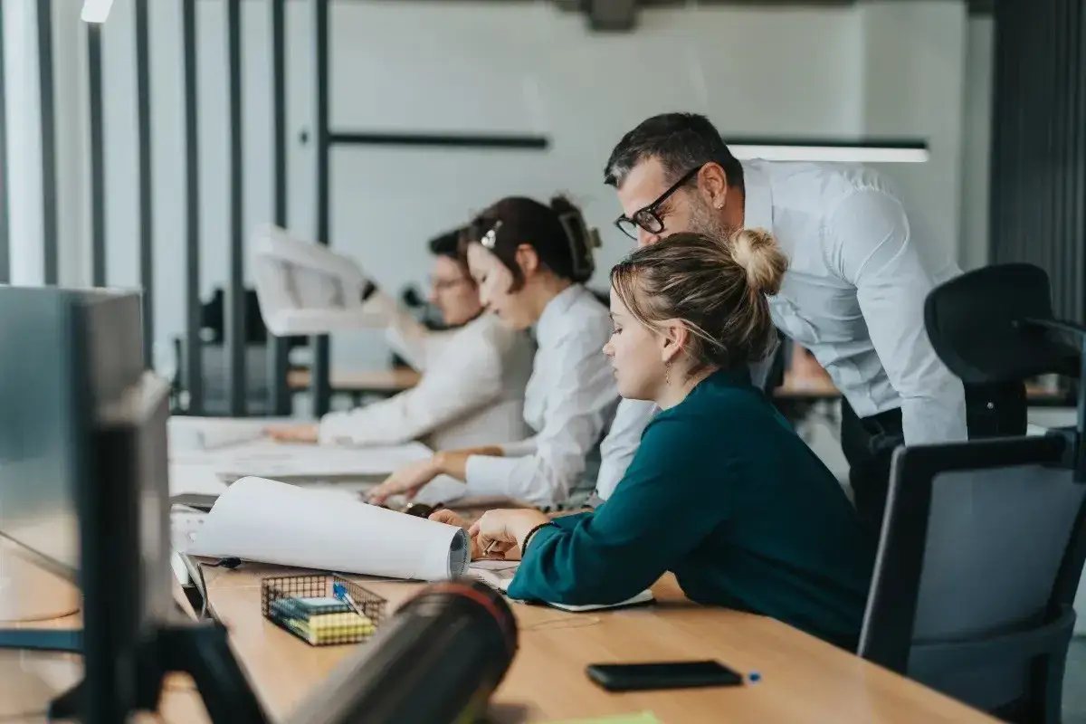 Zespół pracuje nad projektem. Mężczyzna pochyla się nad kobietą, wyjaśniając coś. To przykład, co to jest pracownik najemny.
