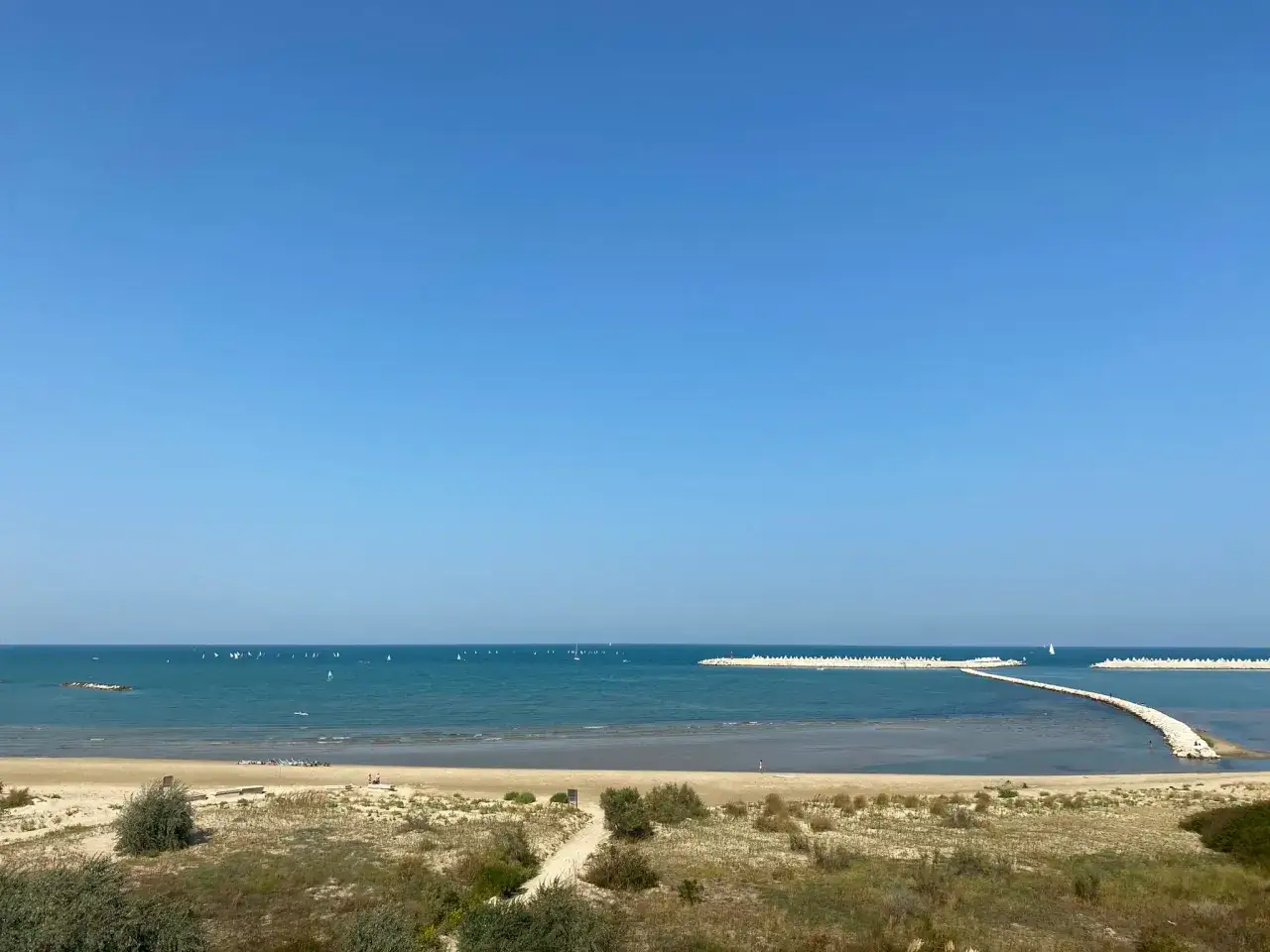 Piękny dzień nad morzem w Pescara i okolice. Wiele żaglówek na turkusowej wodzie, piaszczysta plaża i falochrony.