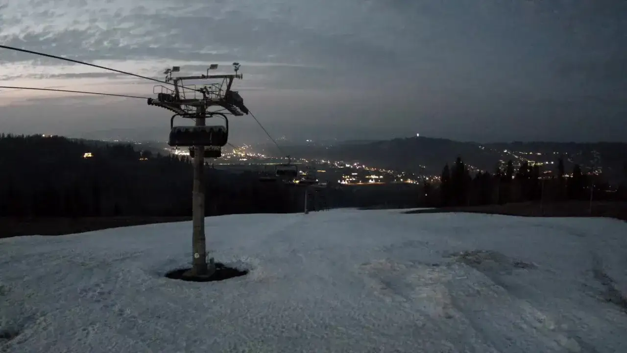 Widok z bukowina ski kamery na ośnieżony stok i nocne światła miasta w oddali.