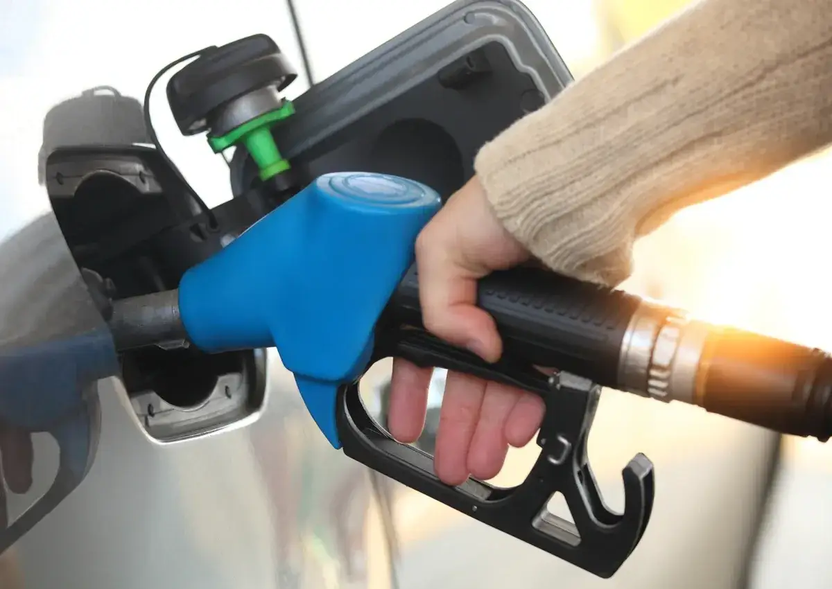 Dłoń trzymająca niebieski pistolet do tankowania paliwa przy samochodzie.