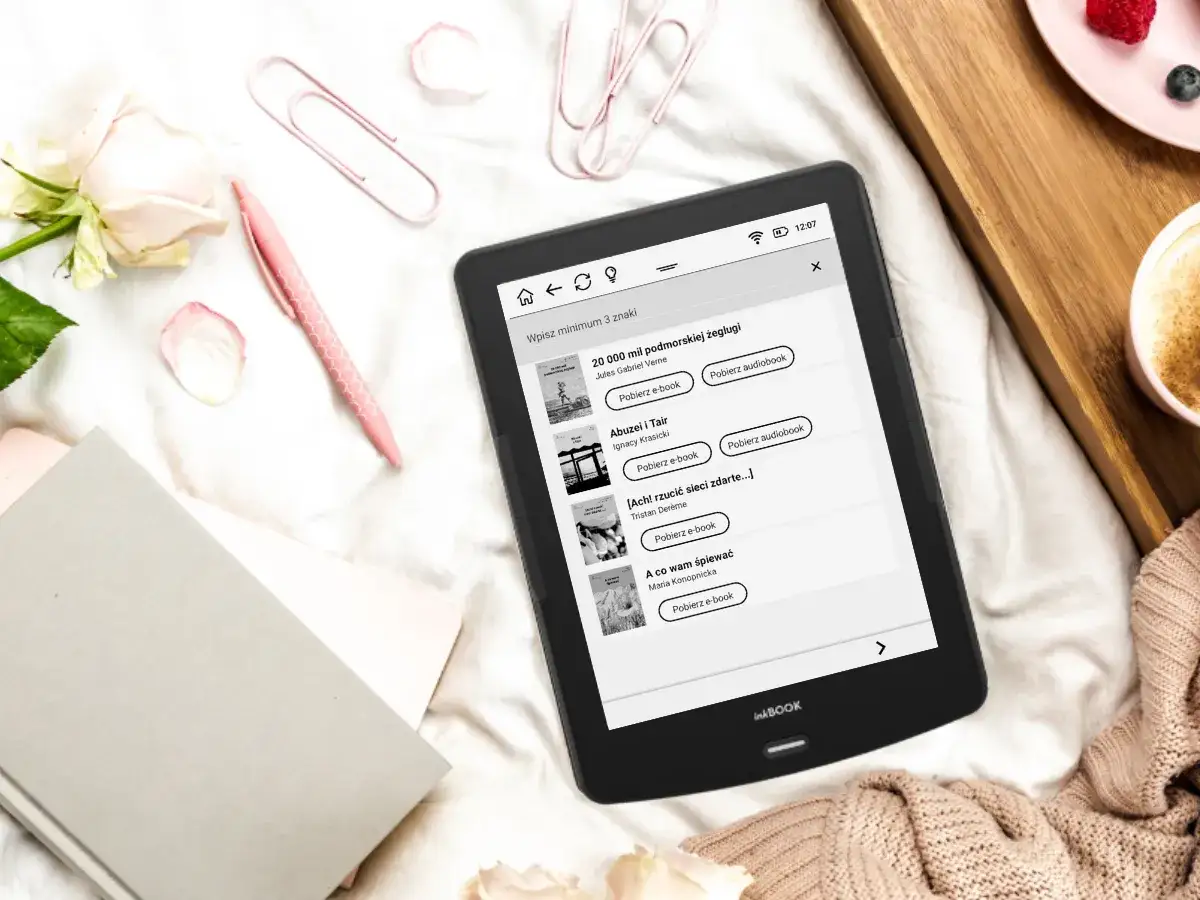 Czytnik ebooków z listą darmowych lektur i audiobooków, obok róż i filiżanka kawy.