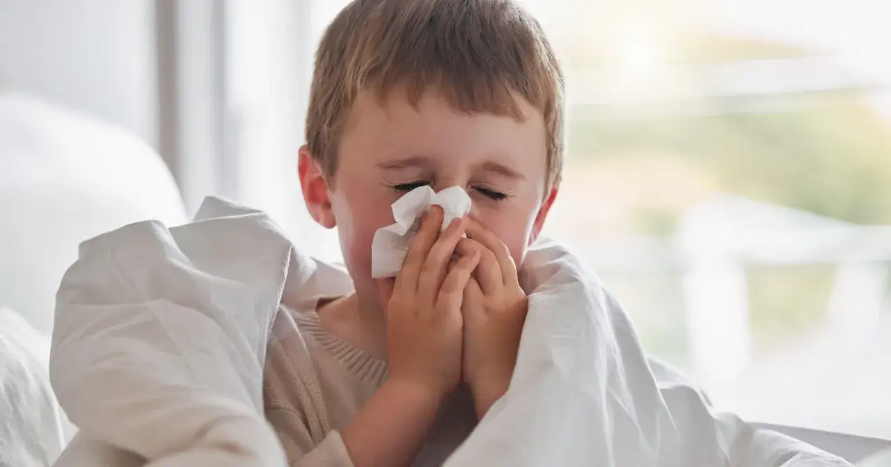 Chory chłopiec z chusteczką w rękach, otulony kocem.