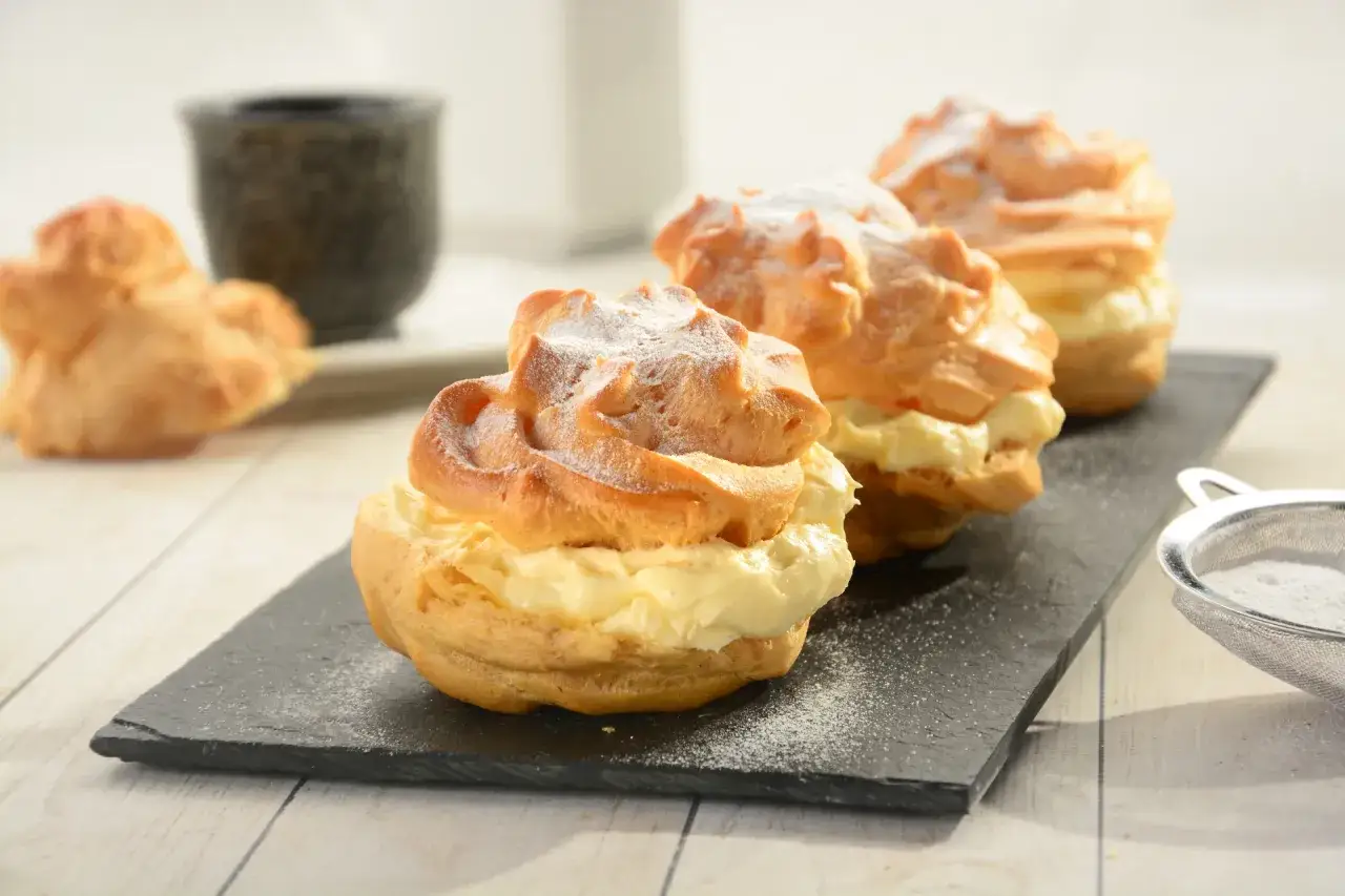 Karpatka a ptysie z kremem, puszyste ciastka przekładane kremem, posypane cukrem pudrem.