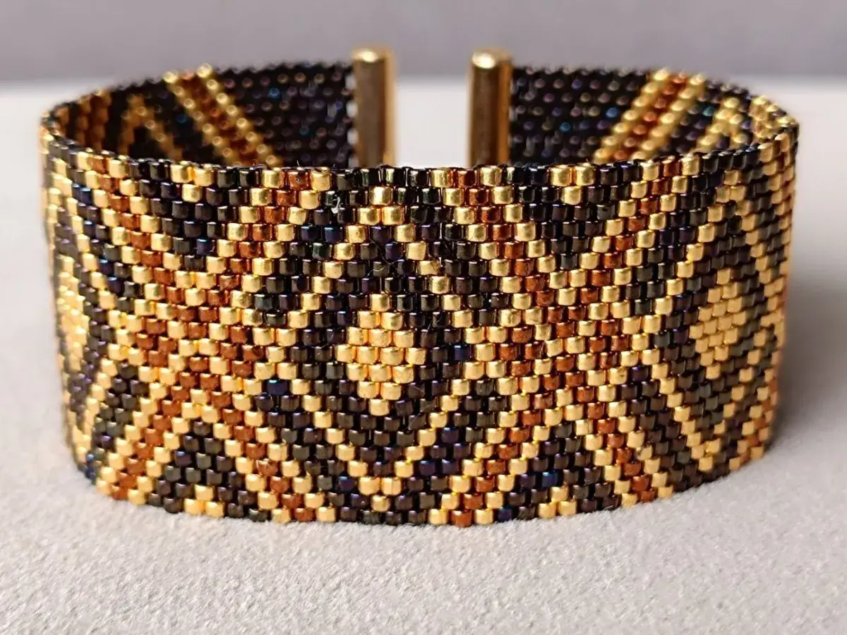 Szeroka bransoletka z koralików w złoto-brązowo-czarne wzory. Inspiracja na bransoletki z koralików, idealna na elegancką biżuterię.
