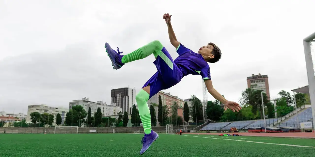 Chłopiec w stroju piłkarskim wykonuje akrobatyczne kopnięcie na boisku.