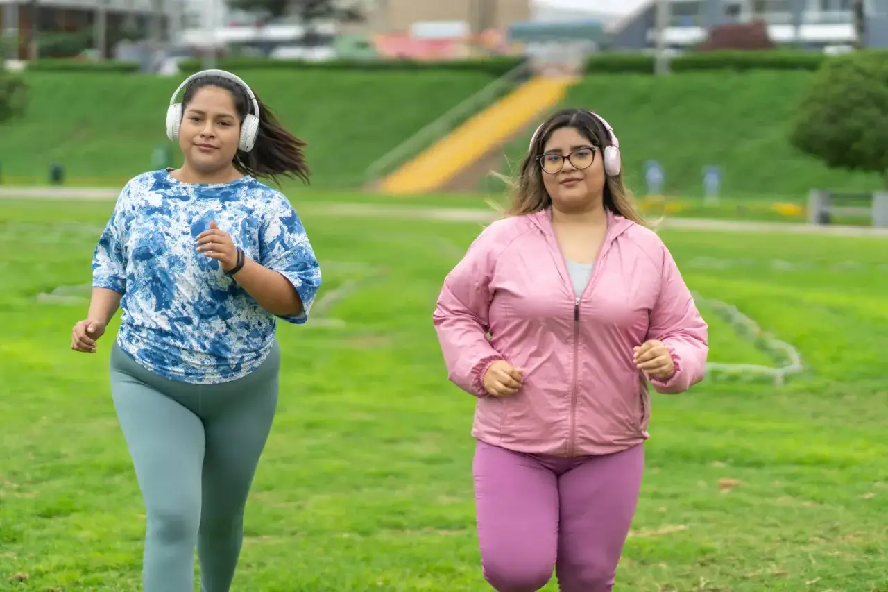 Dwie kobiety w słuchawkach biegają po trawiastym parku.