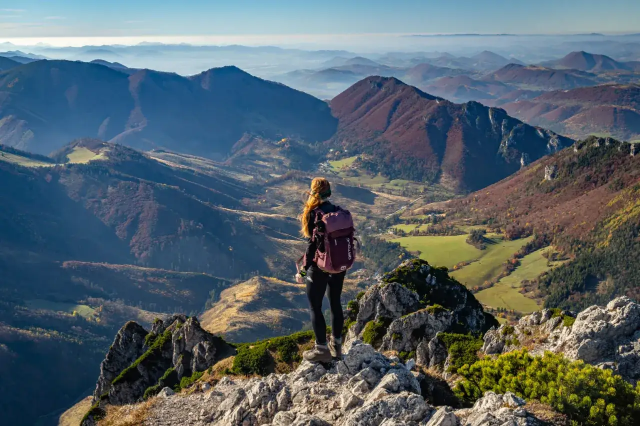 Widok na jesienne pasmo górskie Mała Fatra. Kobieta z plecakiem podziwia panoramę z kamienistego szczytu.