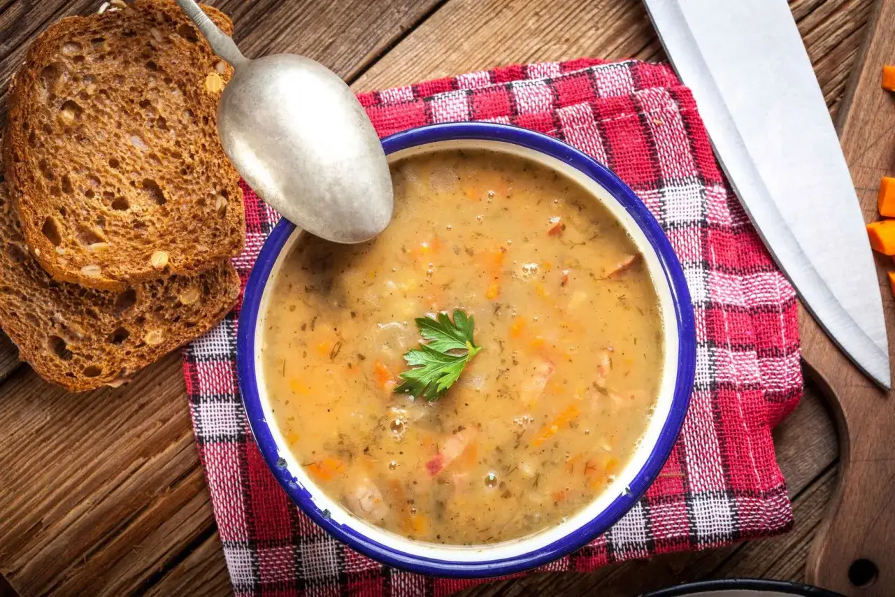 Miseczka grochówki z przyprawą do grochówki, podana z chlebem i łyżką.