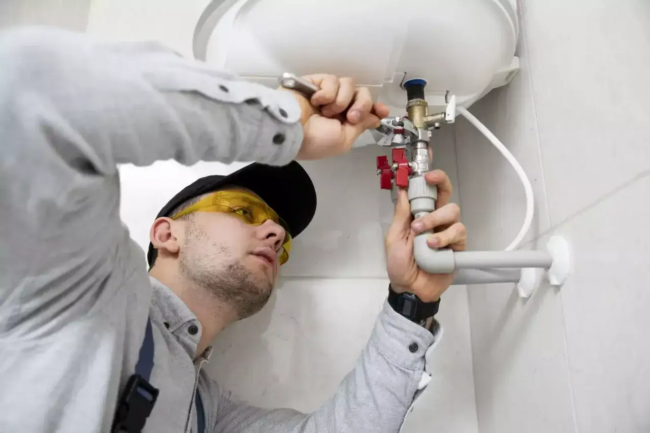 Instalator w okularach ochronnych podłącza bojler, używając narzędzi i rur.