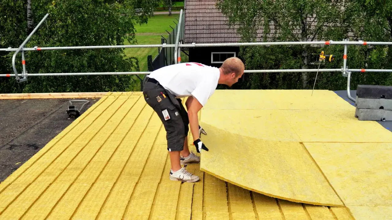 Pracownik układa płyty izolacyjne na dachu płaskim.