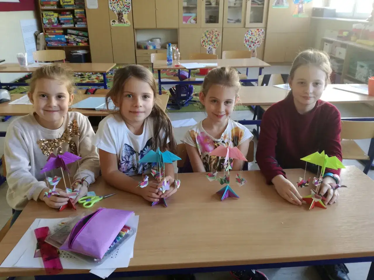 Cztery dziewczynki siedzą przy biurku i trzymają w rękach kolorowe origami.