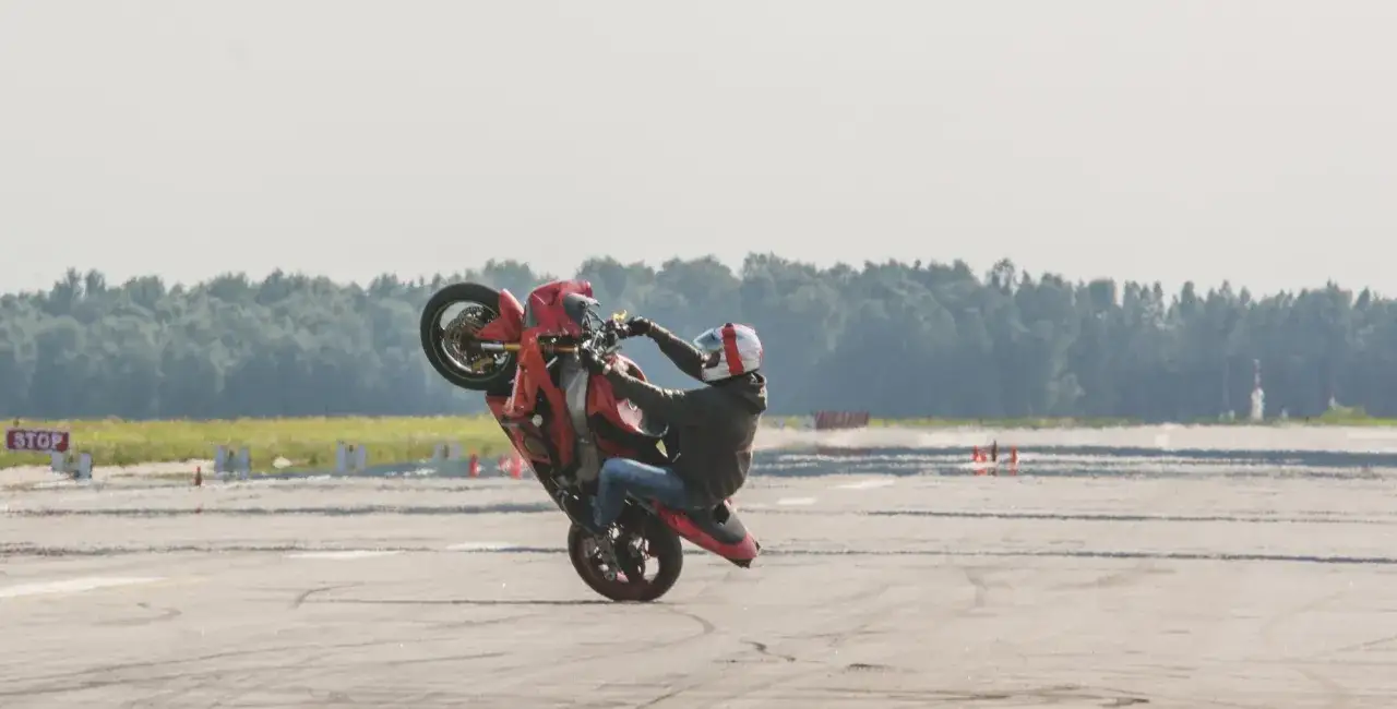 Motocyklista w kasku wykonuje widowiskową jazdę na jednym kole na torze wyścigowym.