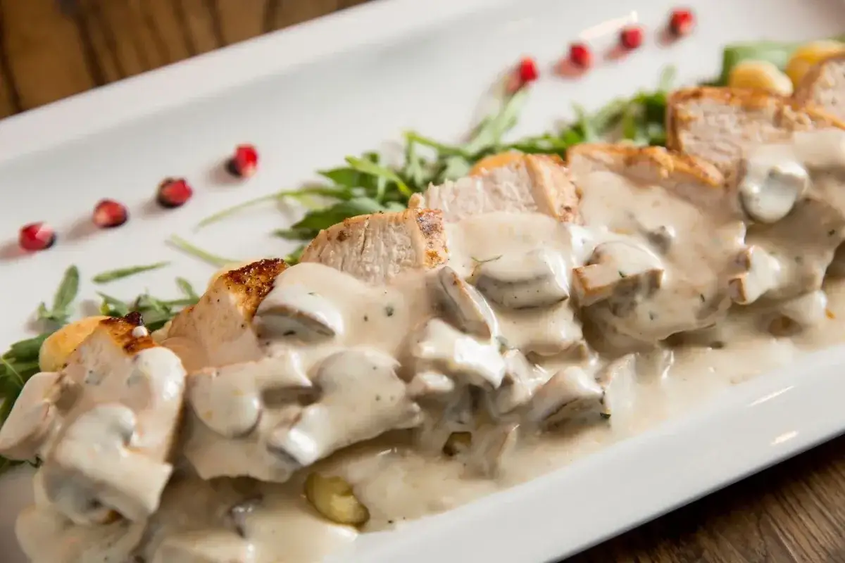 Kawałki kurczaka w kremowym sosie pieczarkowym, idealne do nauki jak zrobić sos pieczarkowy. Podane z rukolą i pestkami granatu.
