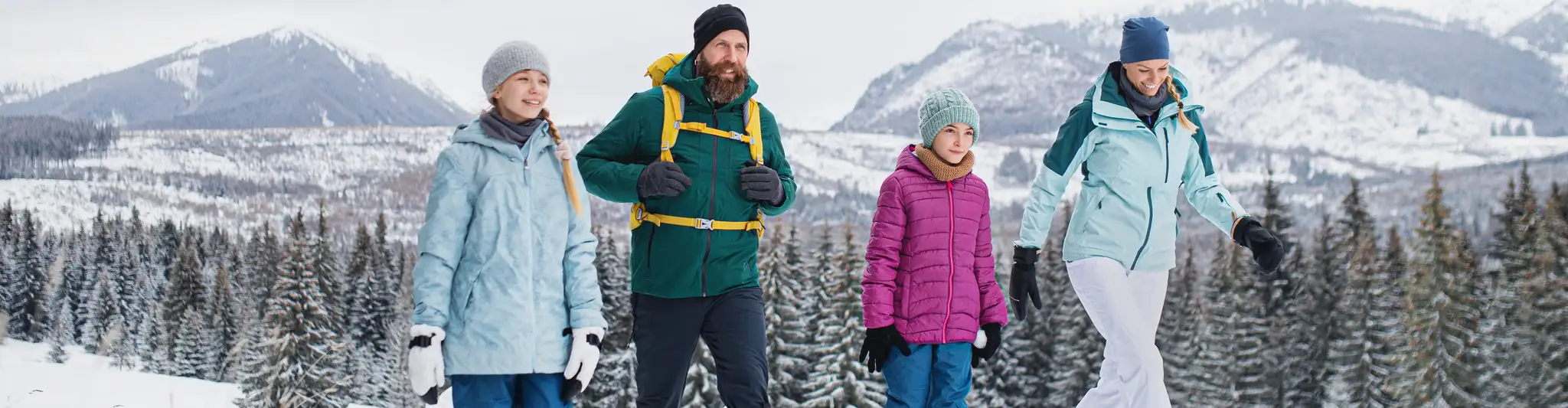 Rodzina w zimowych strojach, pokazująca, jak się ubrać w góry zimą. Ciepłe kurtki, czapki i rękawiczki chronią przed mrozem.