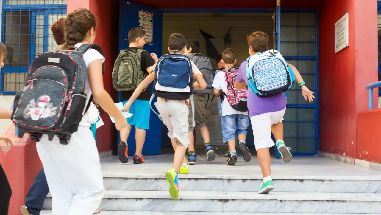 Dzieci z plecakami wchodzą po schodach do szkoły.