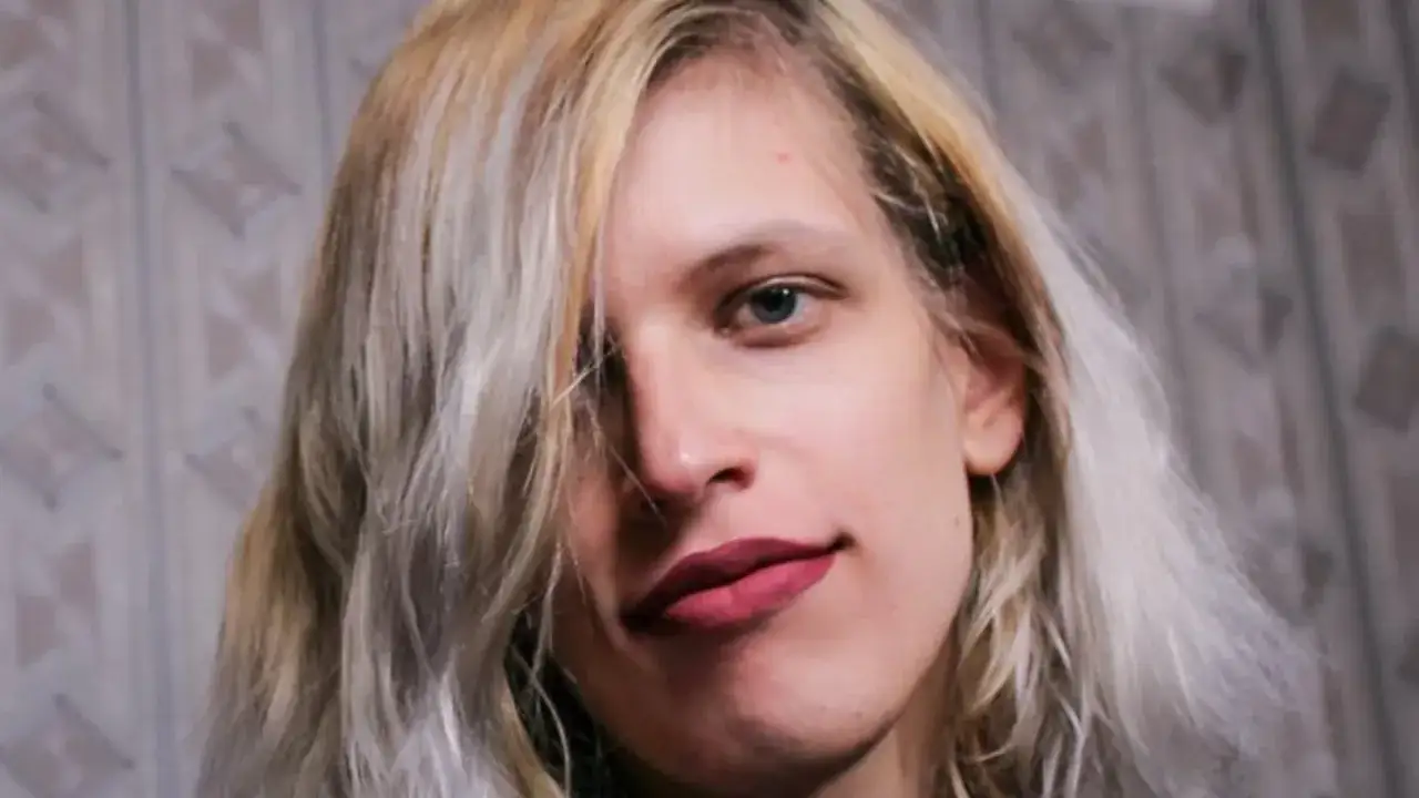 Portret młodej kobiety z blond włosami i niebieskimi oczami. Jej usta są pomalowane na ciemny róż. To pytanie, co to znaczy cis kobieta, jest często zadawane.