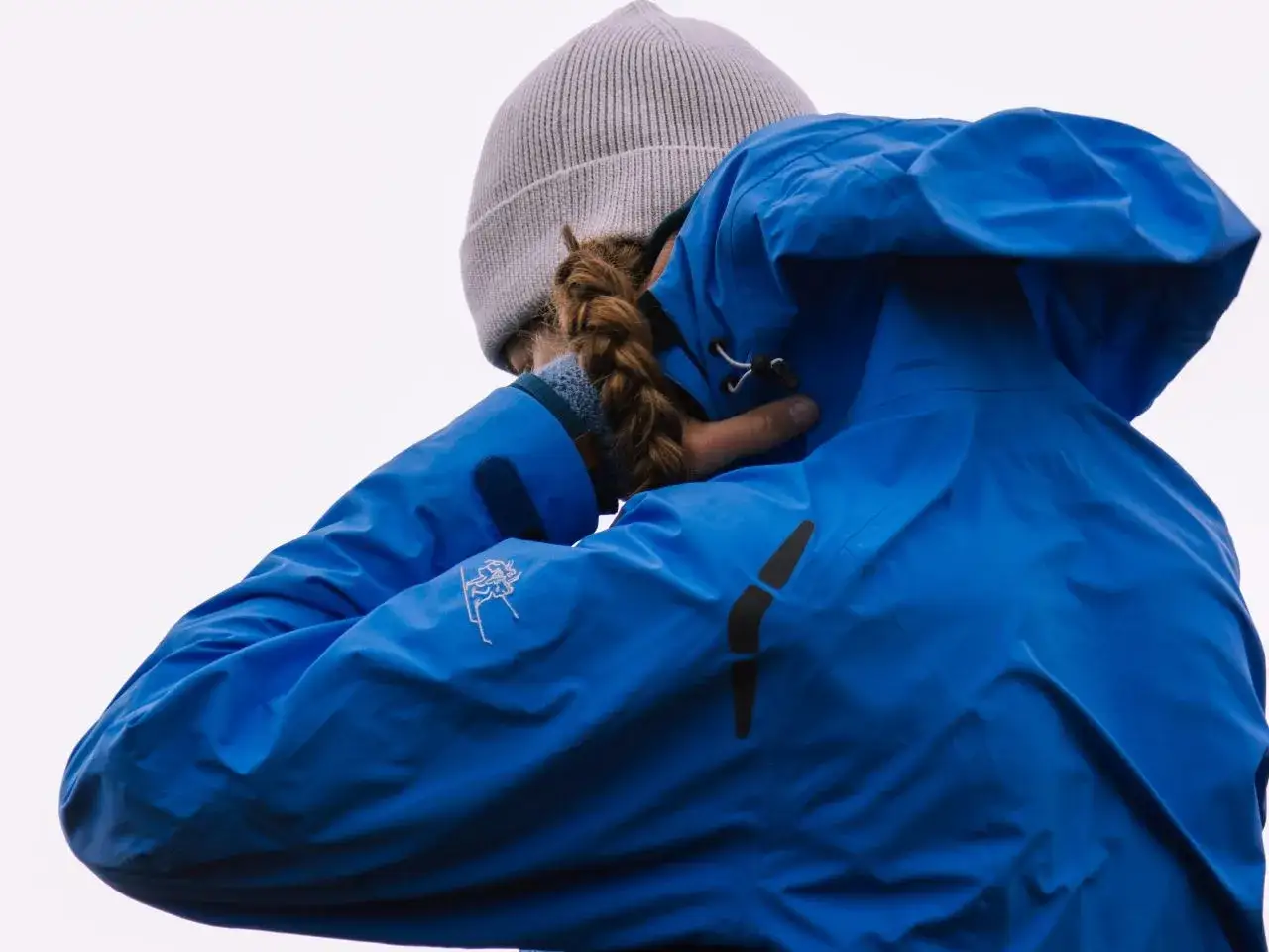 Osoba w niebieskiej kurtce narciarskiej i szarej czapce, z warkoczem.