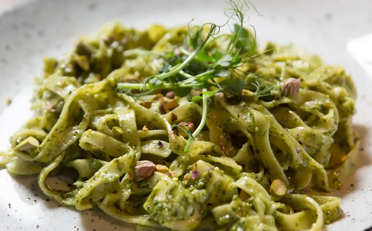 Makaron tagliatelle z zielonym sosem pesto, posypany pistacjami i udekorowany kiełkami.