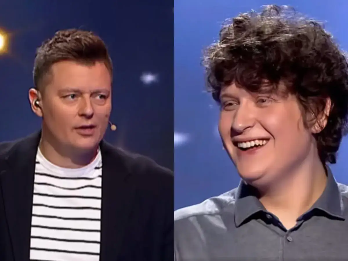 Uśmiechnięty młody uczestnik i prowadzący w okularach na scenie programu "Jaka to melodia finał miesiąca".