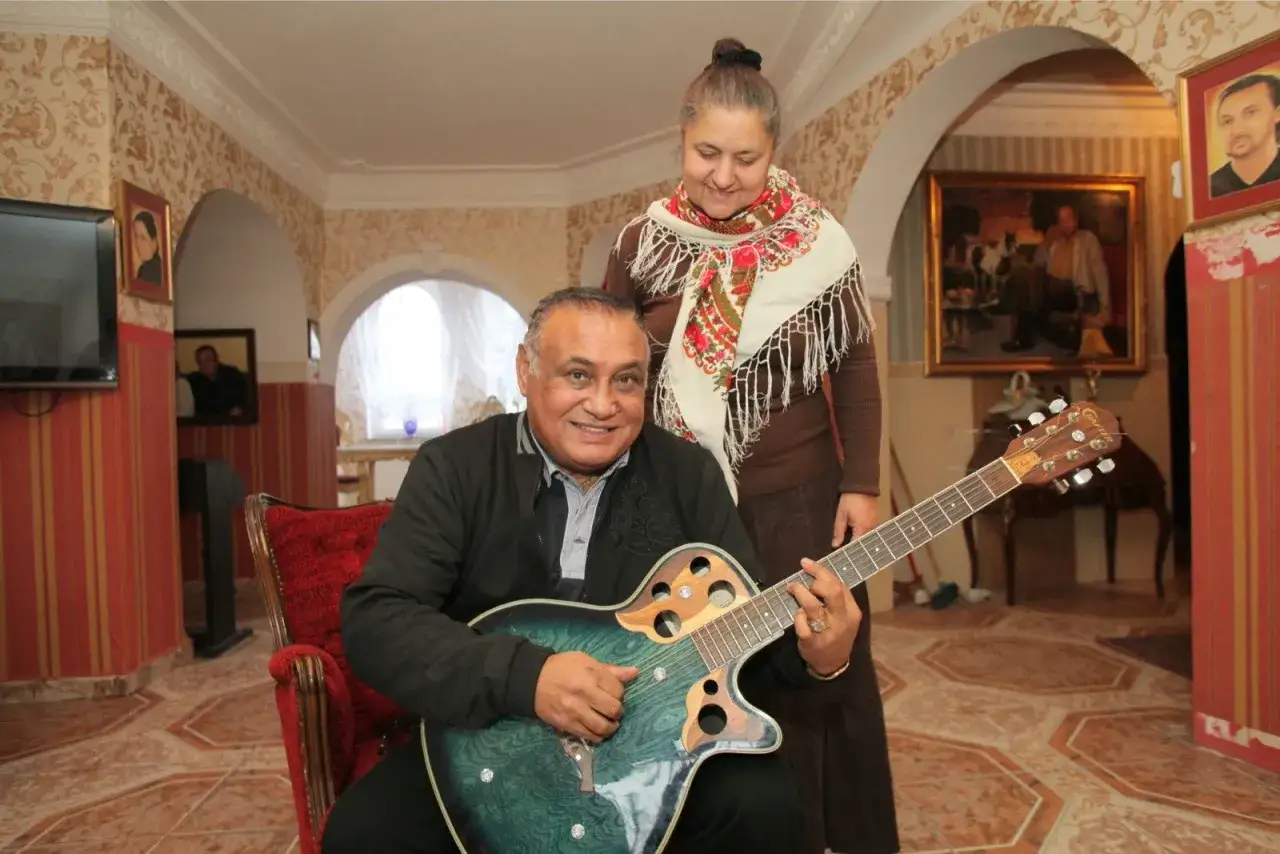 Uśmiechnięty mężczyzna gra na gitarze, a za nim stoi kobieta. Nie wiadomo, ile lat ma Don Vasyl, ale wygląda na szczęśliwego.